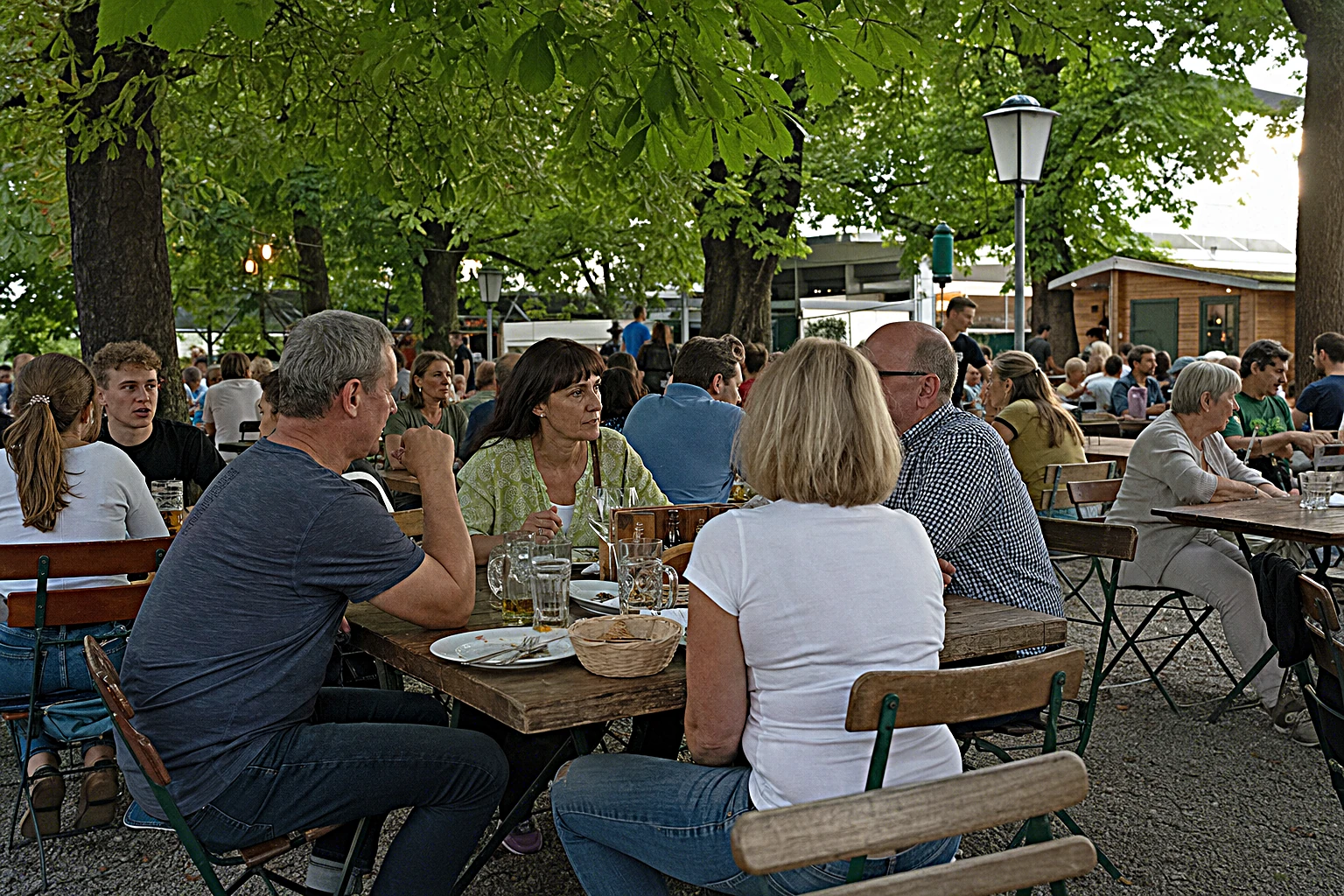 Gut besuchter Biergarten in der Abendsonne mit Gästen an langen Holztischen